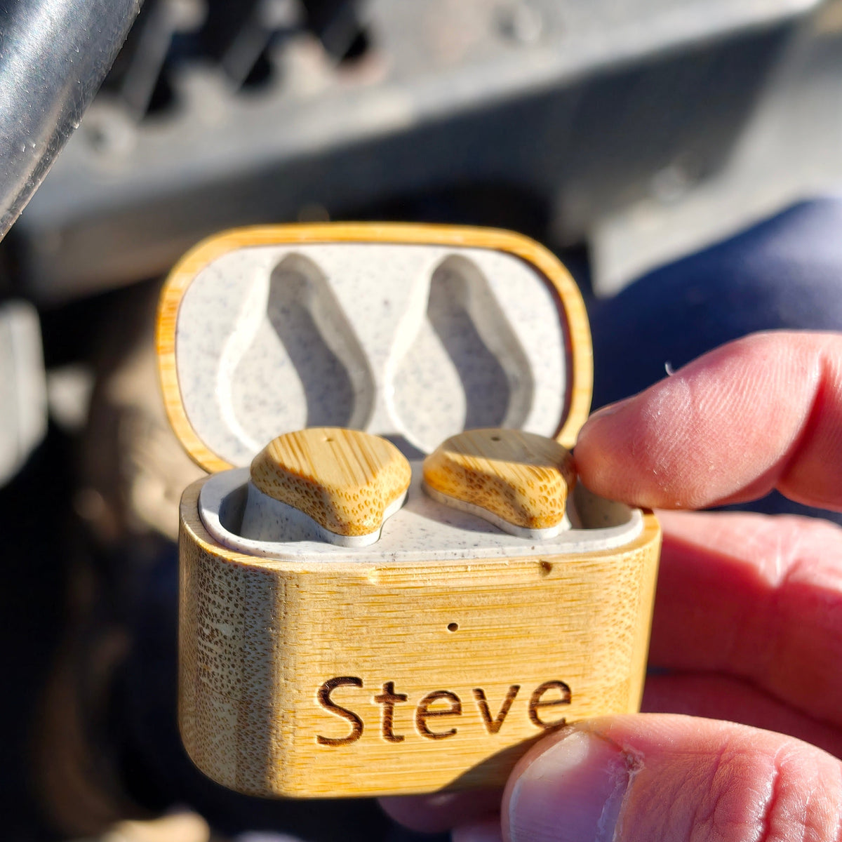 Wooden earbud case with 'Steve' engraved, held by a person outdoors.
