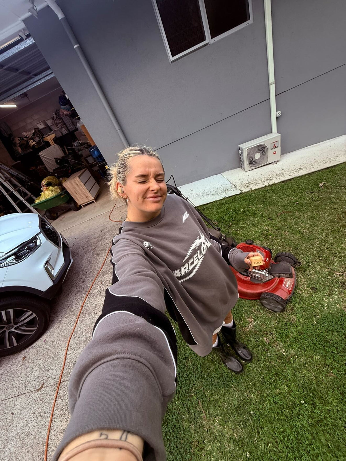 Emily wearing PureBuds Pro earbuds while mowing the lawn, holding the bamboo case engraved with her name