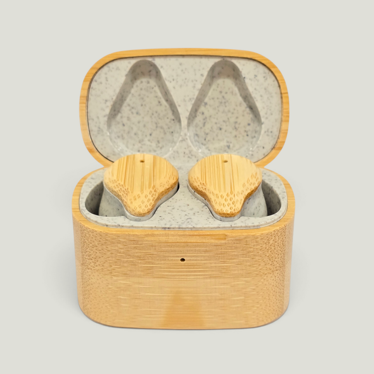 Two natural bamboo wireless earbuds resting inside an open matching bamboo charging case with a wherat straw interior, shown on a light gray background.