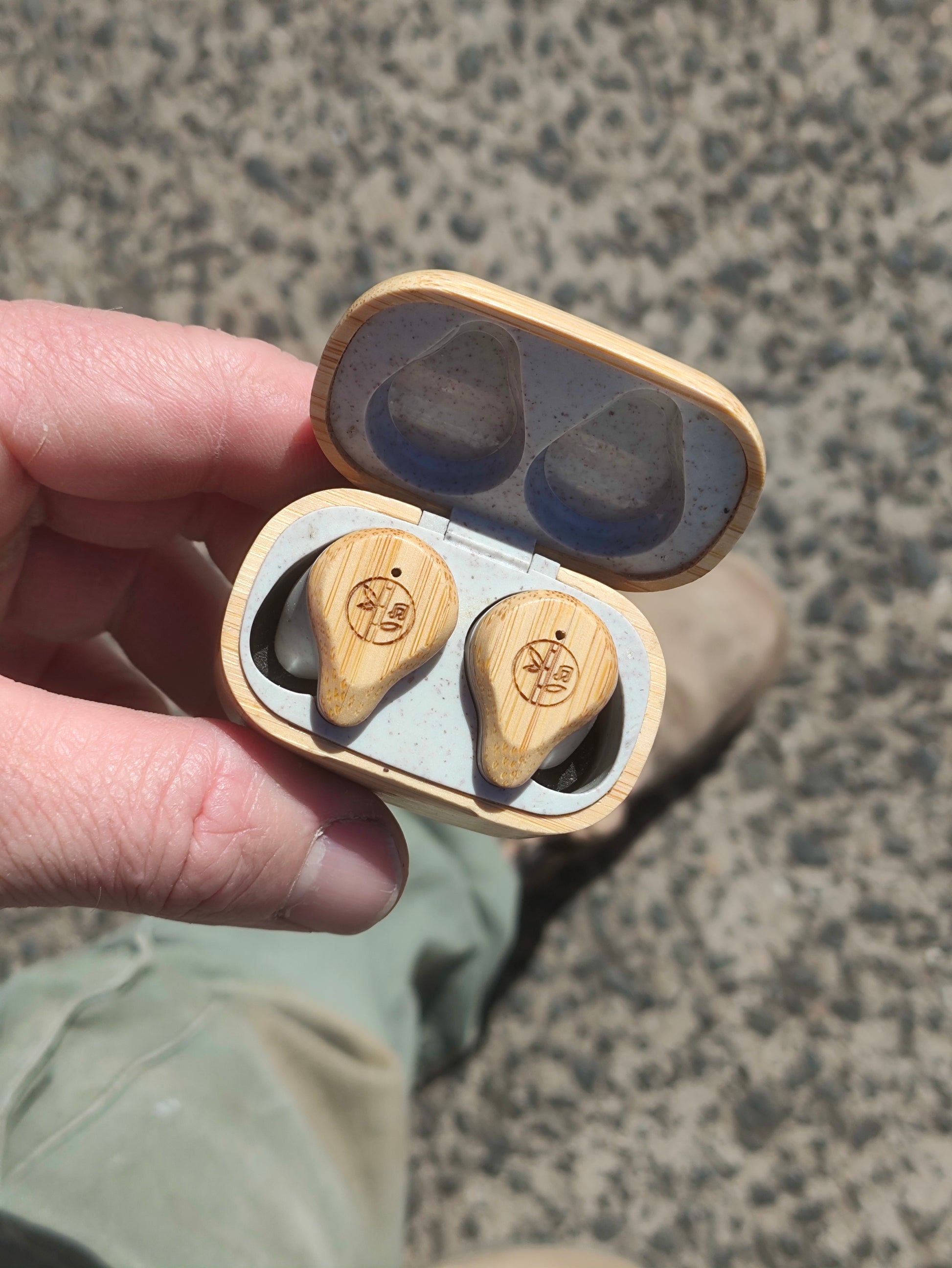 Wooden earbud case with earbuds held by a hand on a textured surface