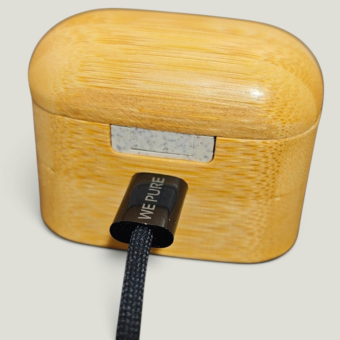 We Pure braided USB-C cable plugged into a light wood grain charging case with laser-engraved connector branding